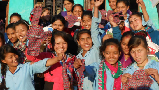 A group of school children stand together in front of their school showing off their new sanitation pads.