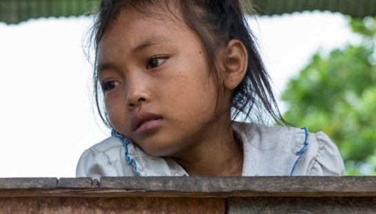 A young child looks over a wooden railing