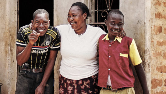 A woman and her two children stand outside their home.