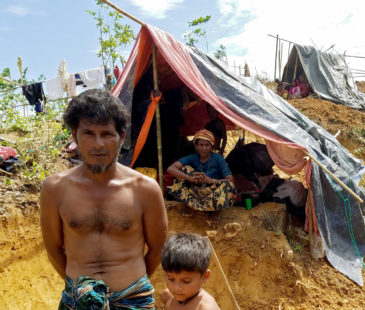 A Rohingyan refugee stands with his son in front of their emergency shelter