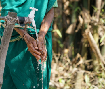 A woman washes her hands at an outdoor tap