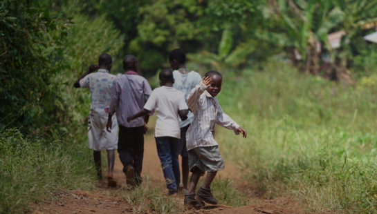 A boy waves as his friends walk along a dirt road