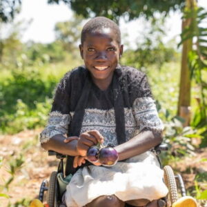 A Ugandan girl in a wheelchair holds two eggplants