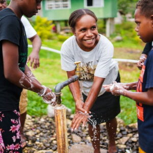 Smiling children stand around a tap, washing their hands