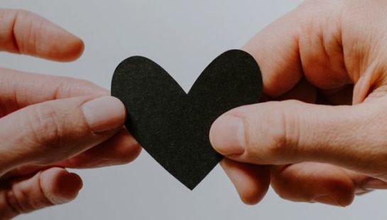 Two hands hold a black cut out paper heart