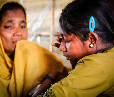 Two Rohingya refugee women sit beside each other and cry