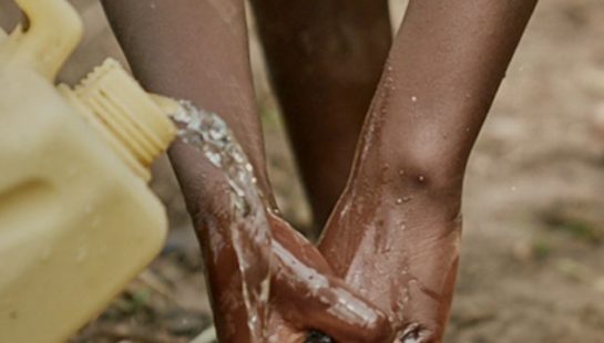 A young girl washes her hands with water