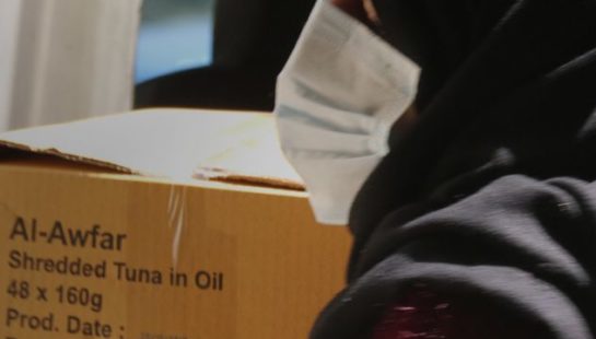 A woman in a hijab holds boxes full of emergency food kits