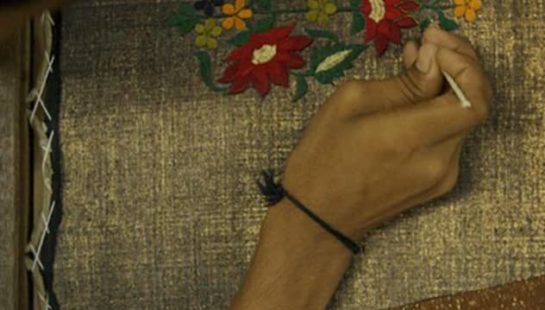 A worker embroiders fabric with red flowers