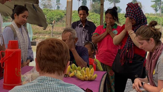 A group of people in Cambodia stand and sit under a make shift tent