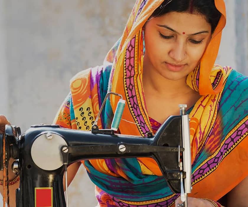 A woman in an orange sari sits at her sewing machine