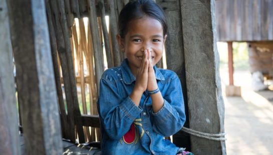 A young Cambodian girl holds her hands together in front of her face