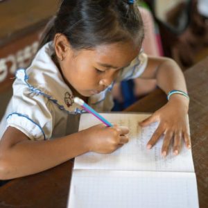 A young Cambodian student takes notes in her school book