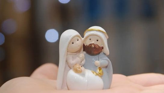 Small figurines of Mary, Joseph and baby Jesus in the palm of a person's hand