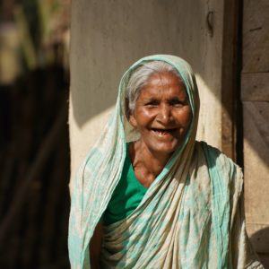 An elderly woman in a turquoise sari smiles at the camera