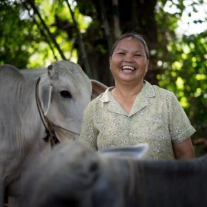 A Cambodian woman smiles in front of her cow