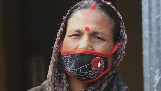 Bangladeshi woman sits in front of her home with a mask on.