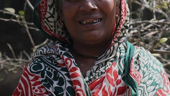 A woman in a colourful scarf stands in front of her fish pond