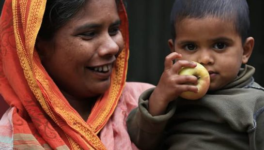 Bangladeshi woman and her baby stand outside a building.