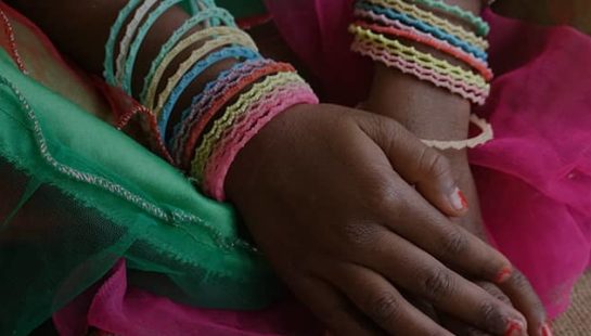A child with colourful bangles on her wrist sits on the floor