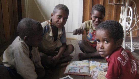 Children in Papua New Guinea sit on the floor reading.