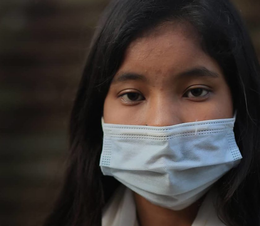 Girl from Bangladesh sits outside with a mask on.
