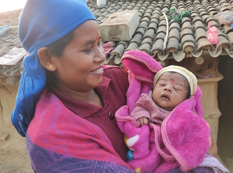 Mother in Nepal stand outdoors with her newborn baby in her arms.