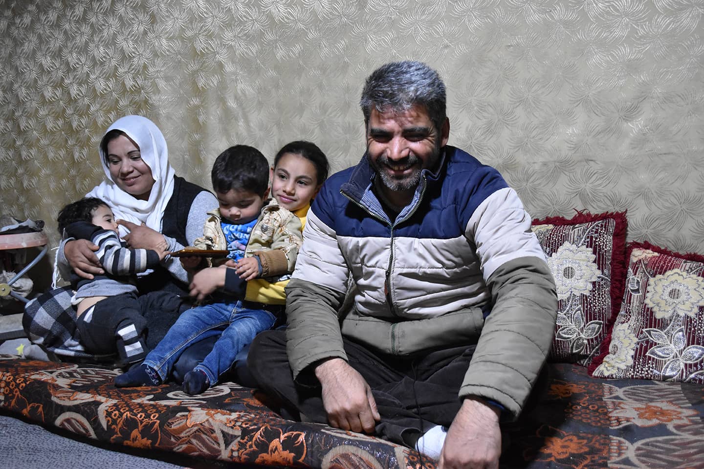 Hamid and his family sit indoors on a mattress.