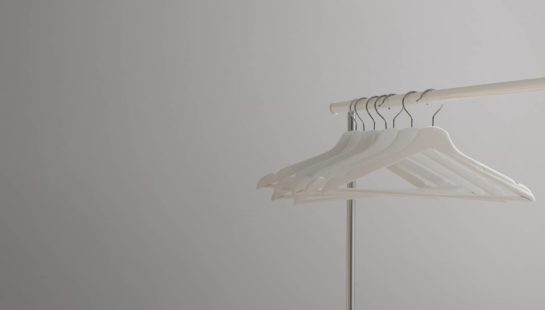 White coat hangers hang on a clothing rack