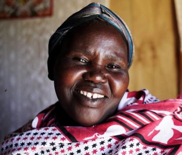 A Kenyan woman smiles to the camera in her home