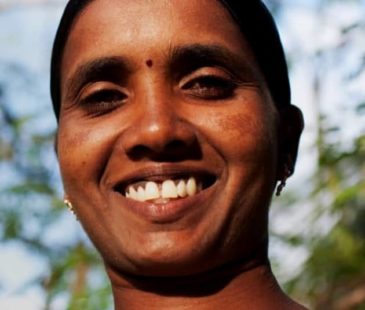 A woman in her vegetable garden smiles