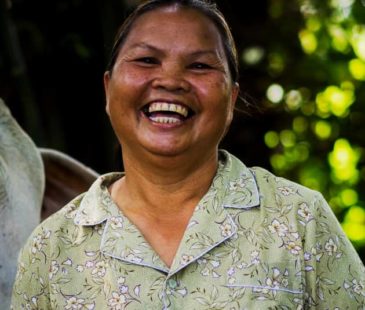 A Cambodian woman in a green floral shirt laughs at the camera