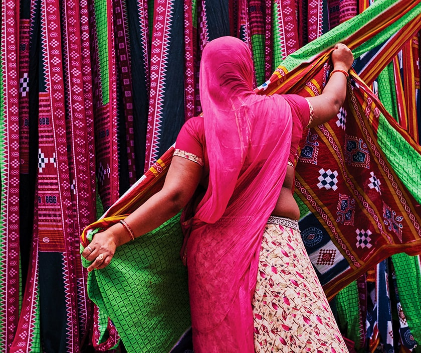 A woman in a sari inspects colourful swaths of fabric.