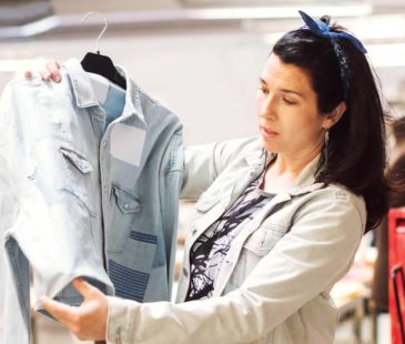 A woman holds up a denim jacket and inspects it