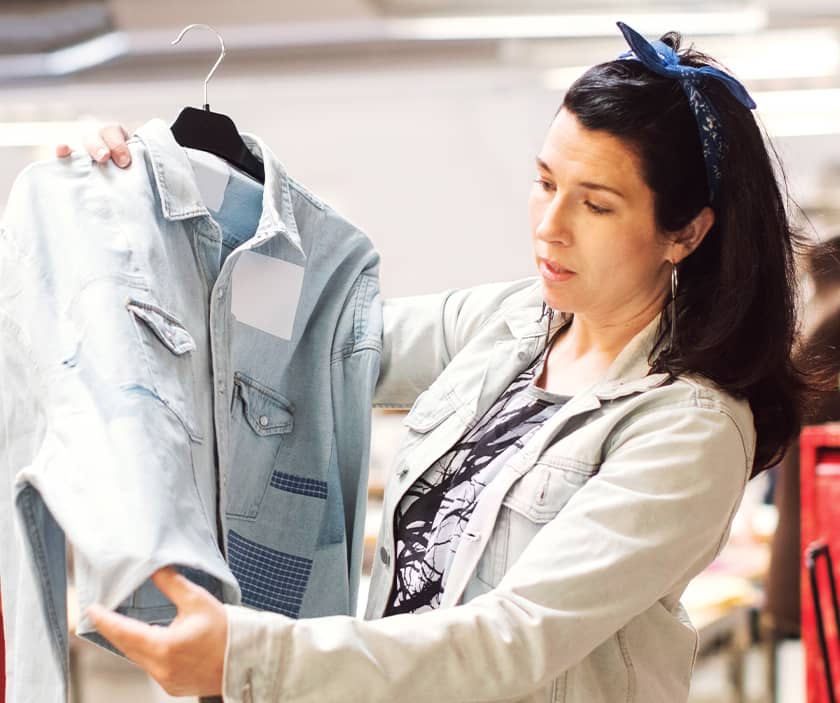 A woman holds up a denim jacket and inspects it
