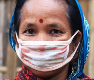 A woman in a blue head scarf wears a cloth face mask