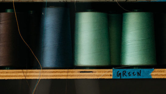 Different colours of thread spools sit on wooden shelves
