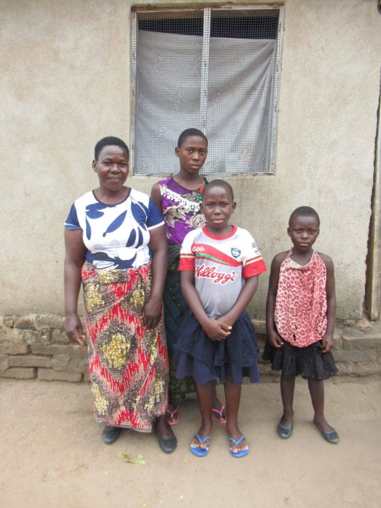 Pacharo, a Malawi woman, stands with her three children outside a taupe building