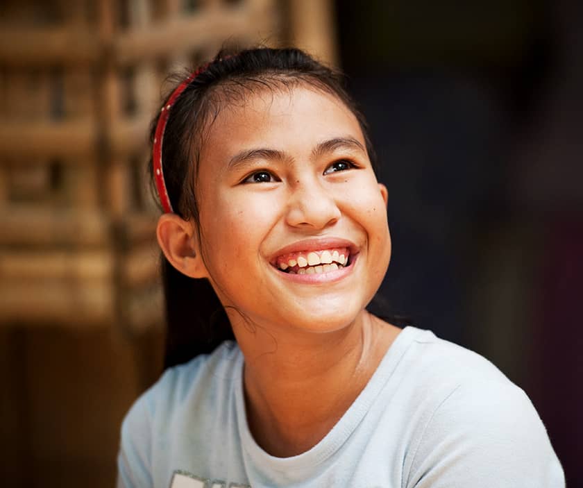 A young Filipino girl wearing a red headband and a white shirt looks up at someone while smiling