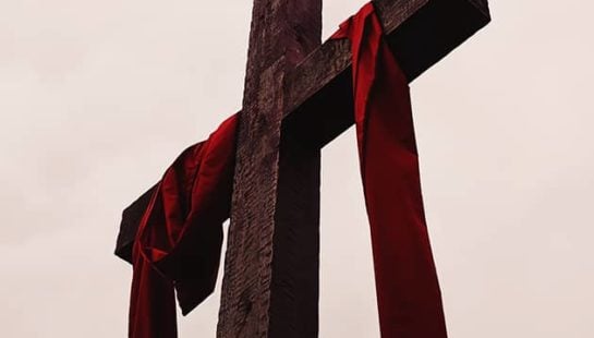 A wooden cross with a red cloth draped around the arms