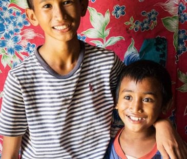 A boy and his younger brother embrace in front of a colourful fabric cloth