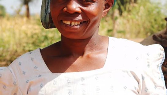 A woman in white and a green head wrap smiles