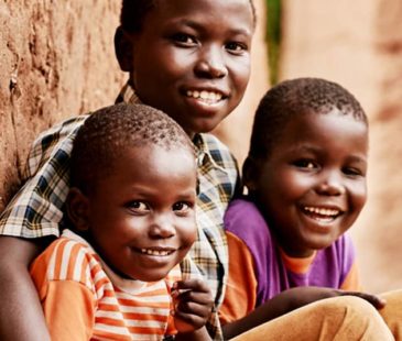 Three siblings from Uganda huddle together, smiling