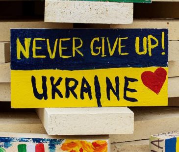 A stone painted as a Ukraine flag with 'Never Give Up! Ukraine' written on it