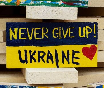A stone painted as a Ukraine flag with 'Never Give Up! Ukraine' written on it