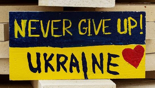 A stone painted as a Ukraine flag with 'Never Give Up! Ukraine' written on it