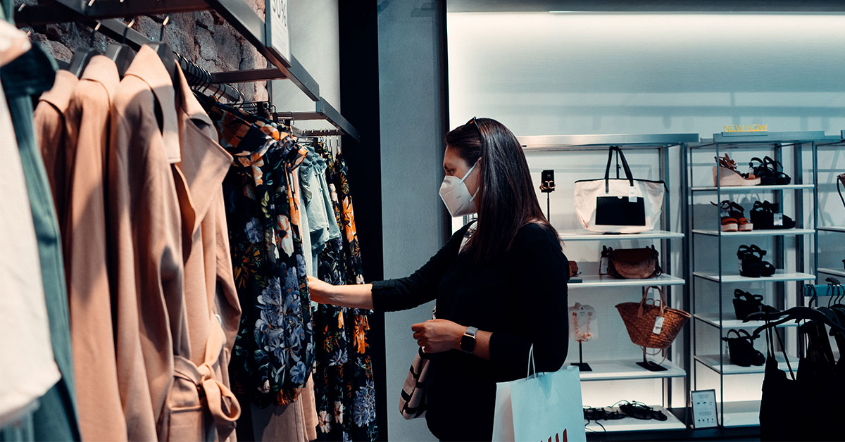 A woman in a cloth masks looks at clothing in a store
