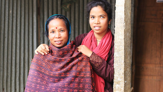 A woman and her daughter stand in front of their home