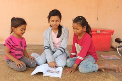 A girl helps two younger girls read a book