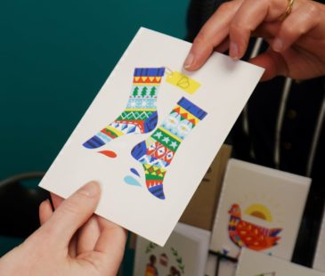 Two hands hold the Better World Gift Christmas Socks Card
